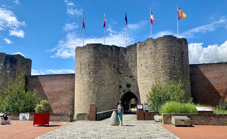 Person standing in front of a historic castle with flags.