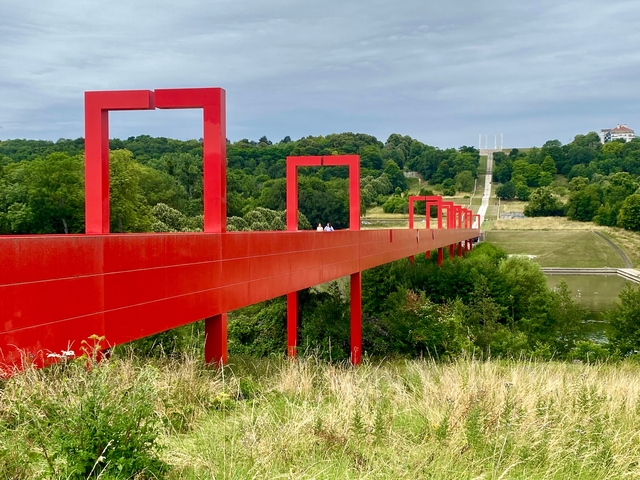 Modern art installation with red frames over a grassy landscape.