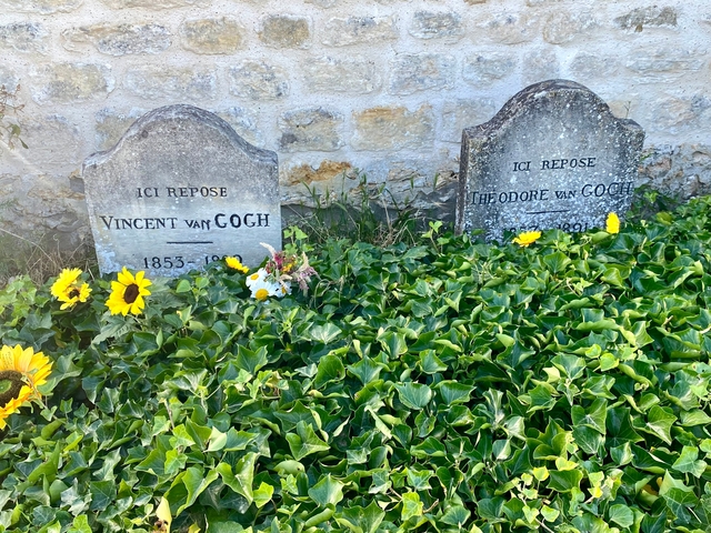 Gravestones of Vincent and Theo Van Gogh surrounded by greenery and flowers.