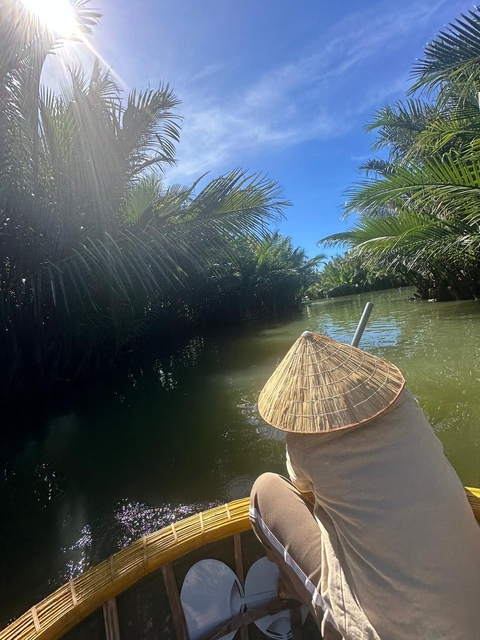 A traditional Southeast Asian conical hat on a boat in a palm-lined river.