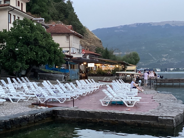 Seaside area with lounge chairs, buildings, and mountains.