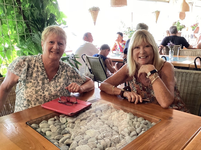 Two women smiling at a table with plants around.