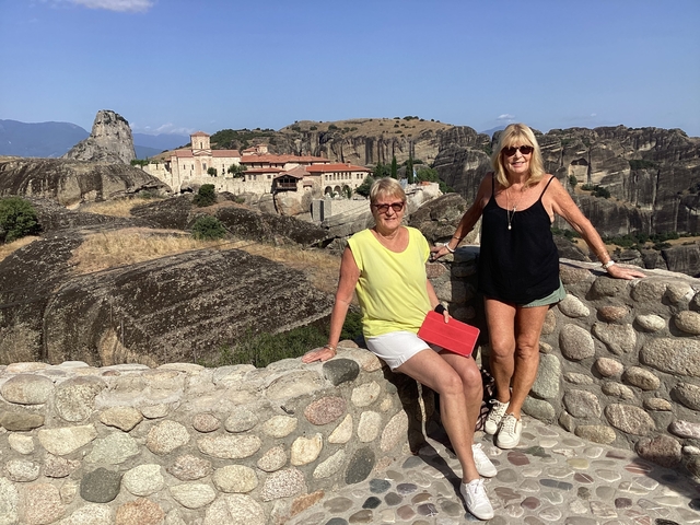 Two women posing on a stone wall with monasteries in the background.