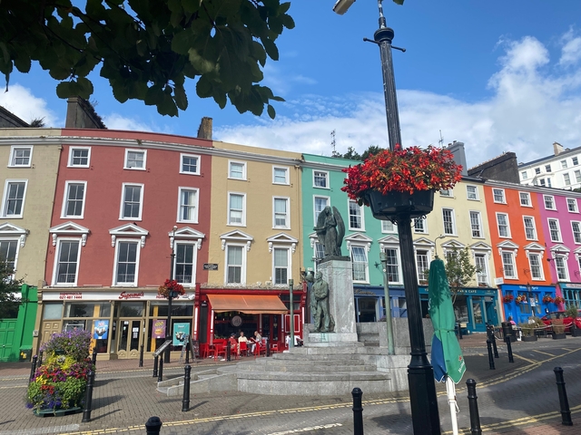 Row of colorful buildings in a city square with a statue and flowers.