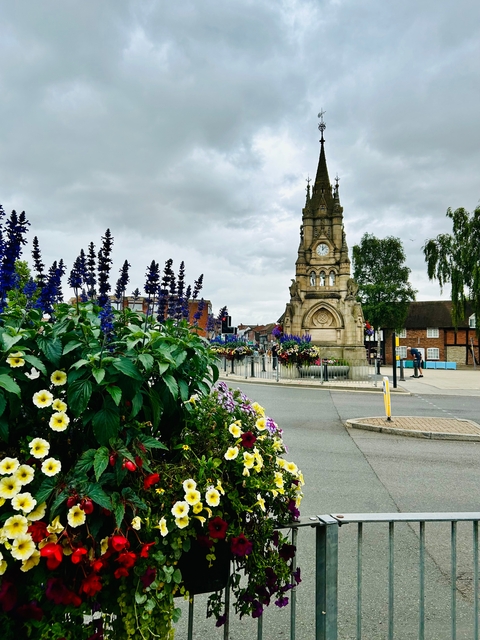 Clock tower surrounded by flowers and greenery.
