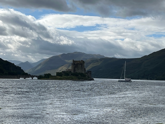 Eilean Donan Castle on the shore of a loch with a sailboat.