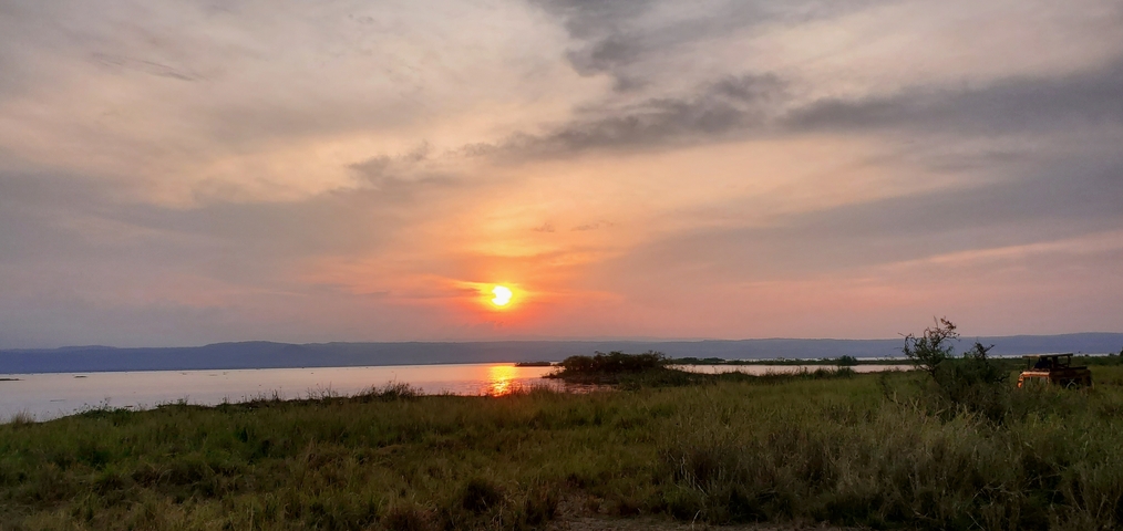 Sunset over a body of water with grassland in the foreground.