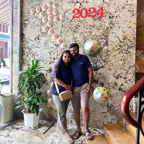 Two people posing indoors with wall decorations.