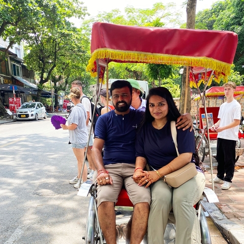 Couple sitting on a rickshaw in a bustling street.