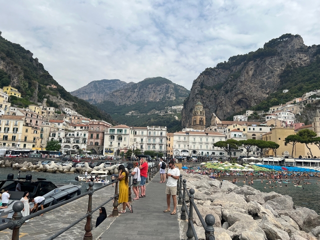 Crowd by the sea with a mountainous coastal city in the background.