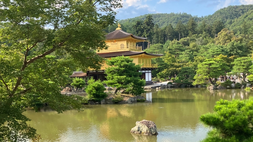 Golden pavilion at the edge of a pond with trees.