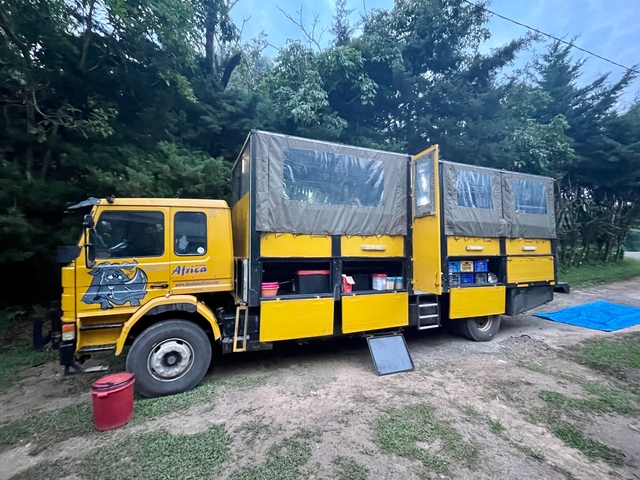 Yellow safari truck with open compartments in a forested area.