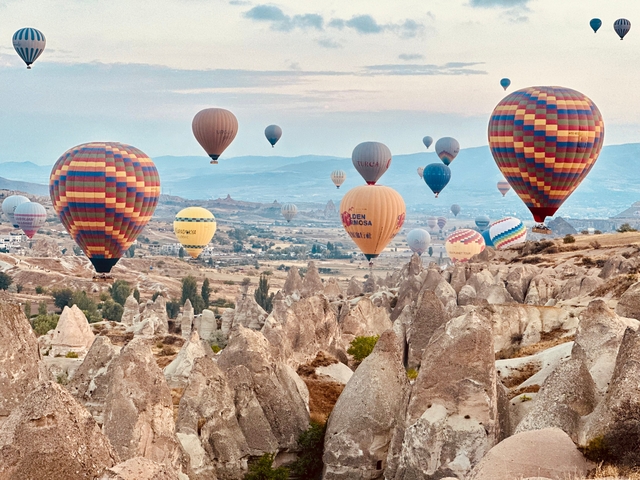 Multiple colorful hot air balloons floating over a rocky landscape.