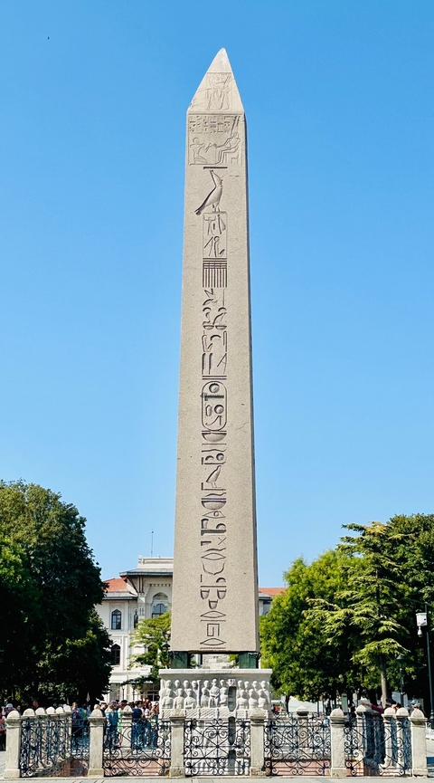 An ancient stone obelisk with hieroglyphs against a clear blue sky.