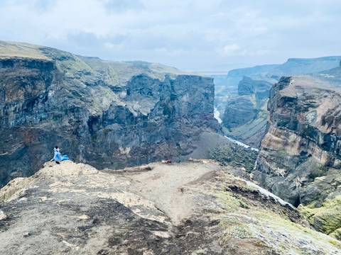 Person sitting on the edge of a dramatic canyon view.