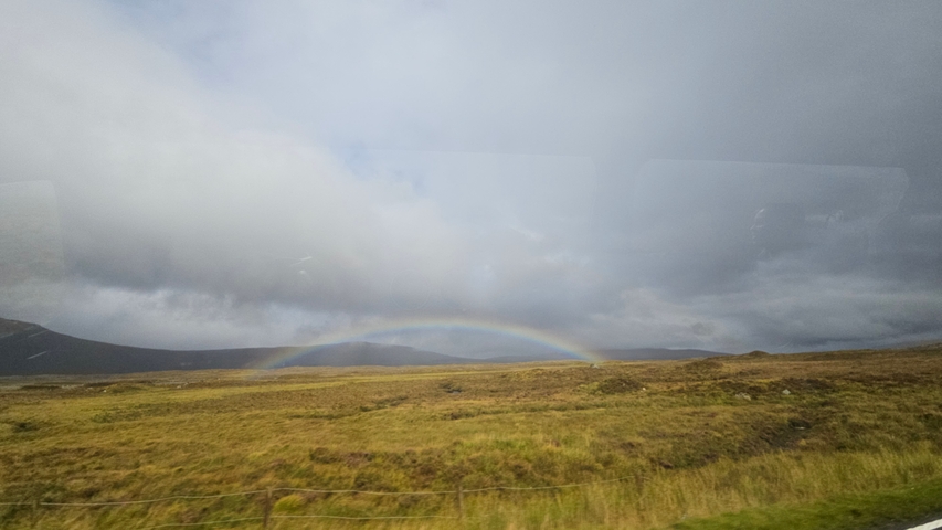 A rainbow over a grassy plain with cloudy skies.