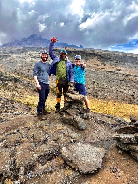 Three people posing with stacked rocks on a mountain.