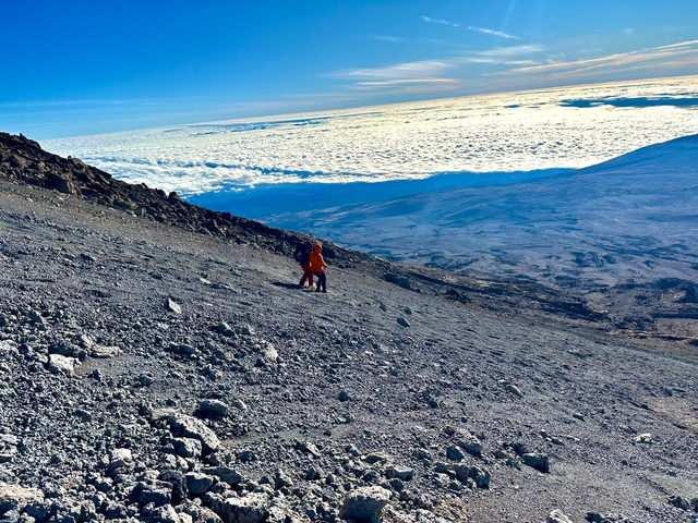Two hikers descending a rocky terrain with a view of clouds.
