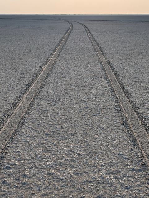 Two parallel tire tracks on a sandy surface.
