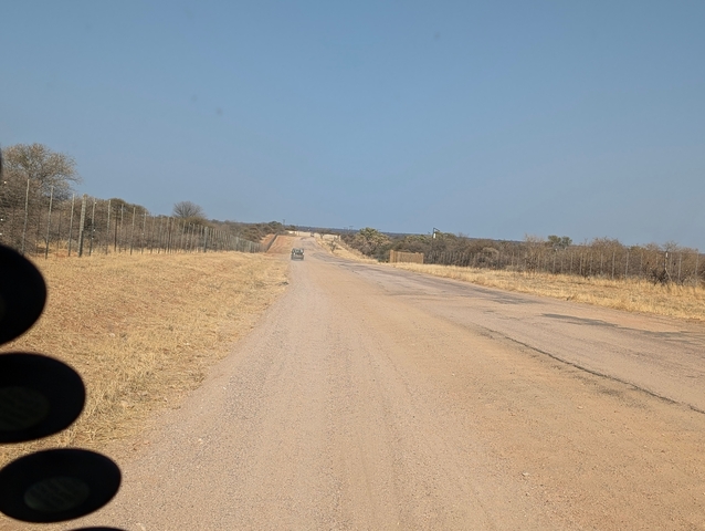 A long, empty road lined with dry grass and a car in the distance.