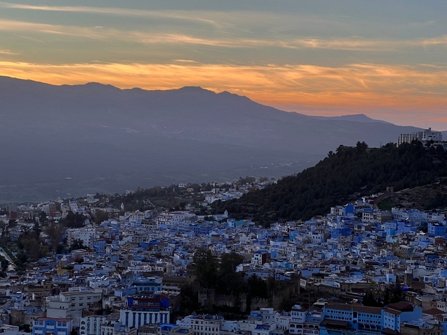 Sunset over a Moroccan town with blue buildings on a hillside.