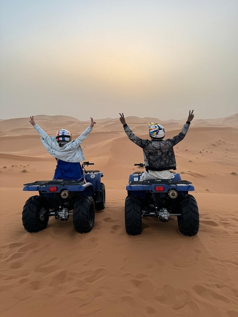 Two people on quad bikes raising their arms in a desert landscape.