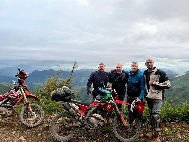 Four people posing with motorcycles in the mountains.