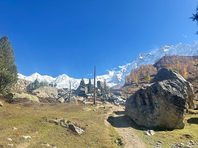 Mountain trail with boulders and snow-capped peaks.