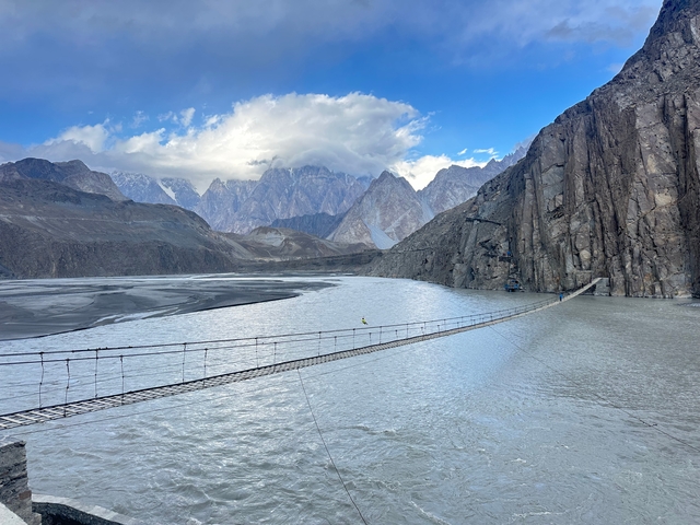 Suspension bridge over a river with mountains in the background.