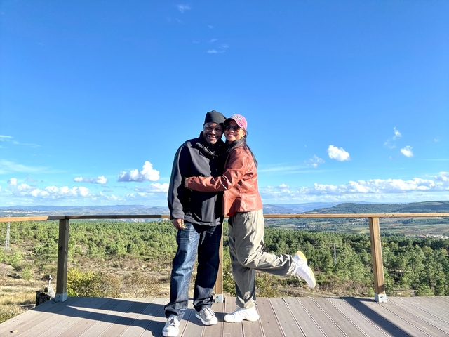 Couple embracing on a wooden deck with a scenic background.