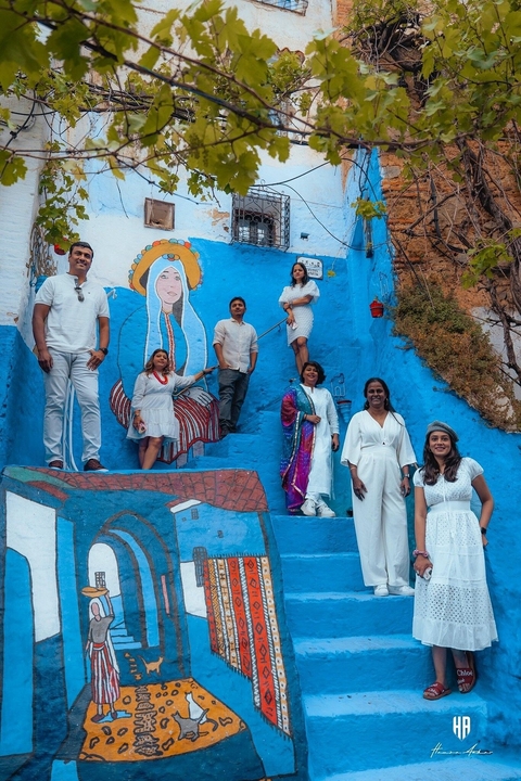 Group of people posed against a mural on a blue street.