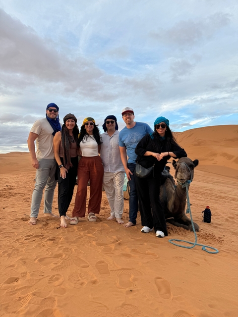 Group of people posing with camels in the desert.