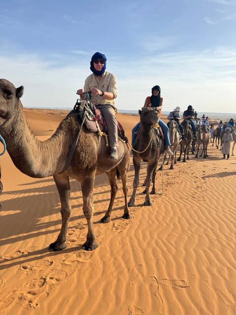 Group of people riding camels in a desert landscape.
