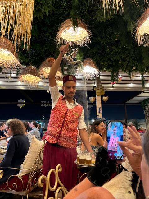 Waiter pouring liquid from a height in a restaurant setting.