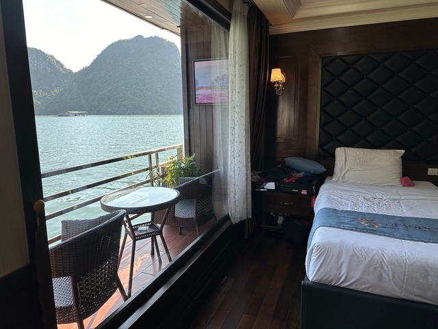 Cozy cruise cabin with bed and balcony overlooks serene emerald waters and limestone karst peaks.