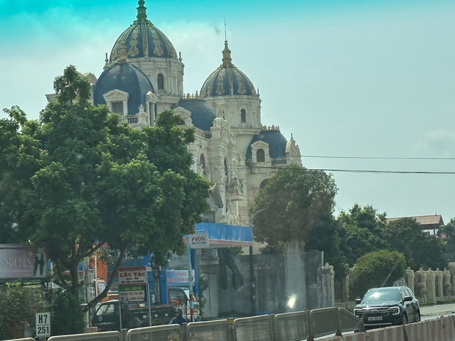 Ornate neo-Gothic style cathedral with blue domes and intricate stonework rises behind roadside trees.
