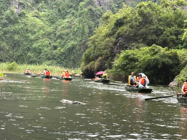Tourists wearing life-jackets are rowed through a narrow river gorge lush with tropical vegetation.
