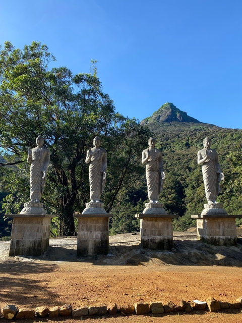 Four statues in front of a mountain peak surrounded by greenery.