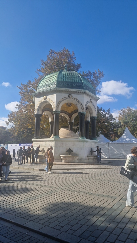 People gathered around a historical pavilion with arches and mosaics.