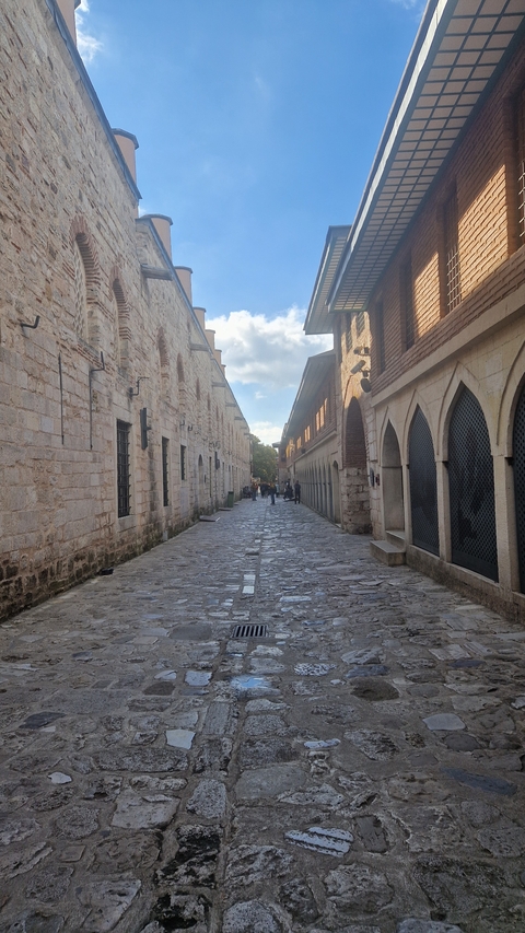 Narrow cobbled street with historical stone buildings and people walking.