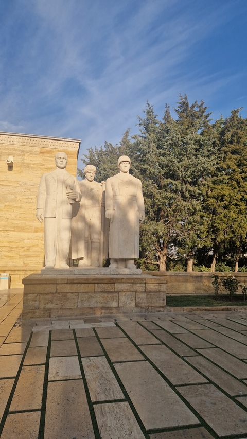 Statues of historical figures in front of a building with greenery around.