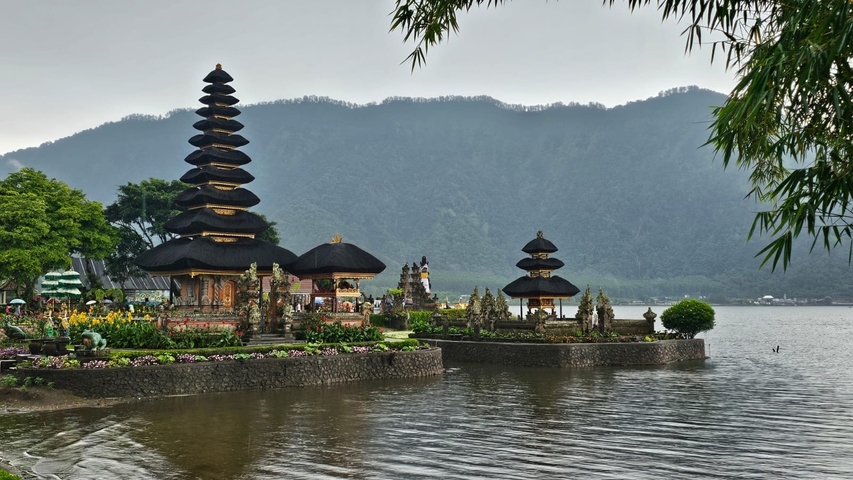 Temple with pagodas by a lakeside with mountains.