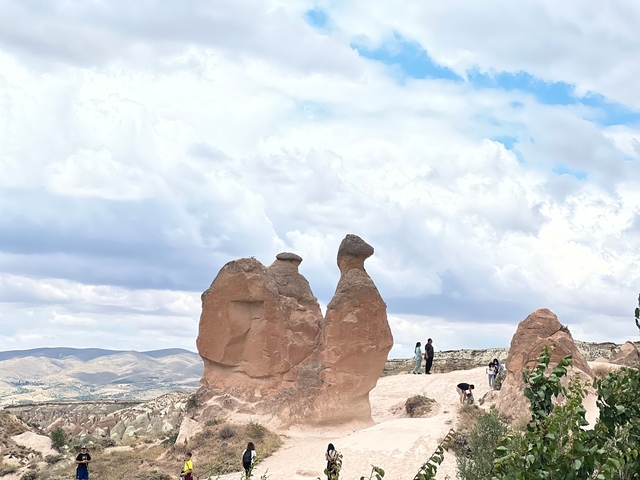 Rock formations under a cloudy sky, people nearby.