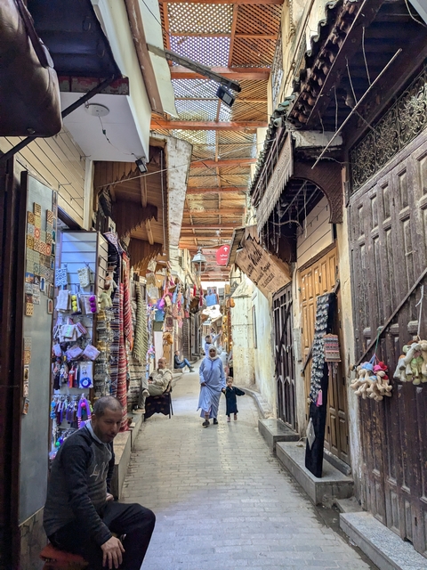 A lively market alley with people shopping and a woman and child walking.