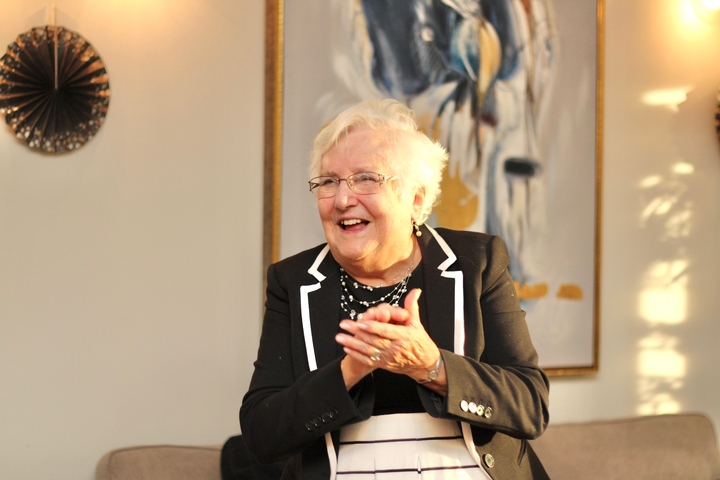 Elderly woman in formal attire clapping, indoors.