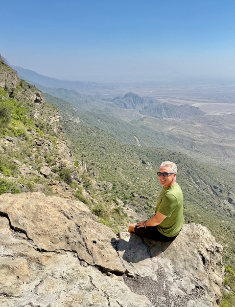 Person standing on a cliff edge overlooking a valley.