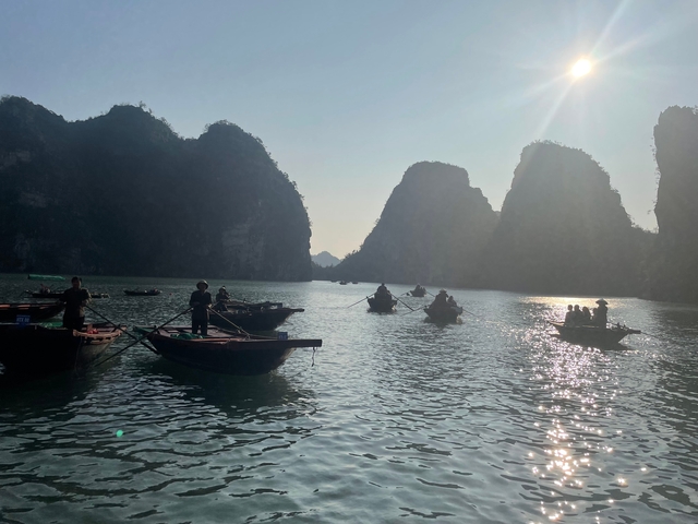 Small boats on a serene body of water with tall limestone cliffs.