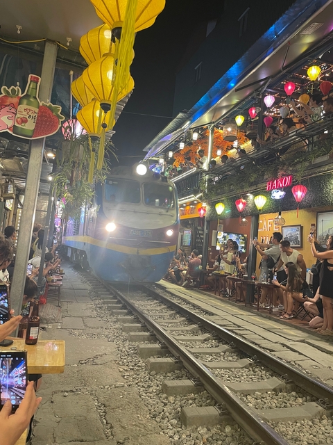 Train passing through narrow street with outdoor cafes.