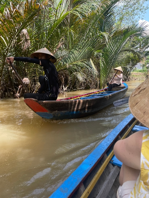 People paddling a wooden boat through a narrow waterway.