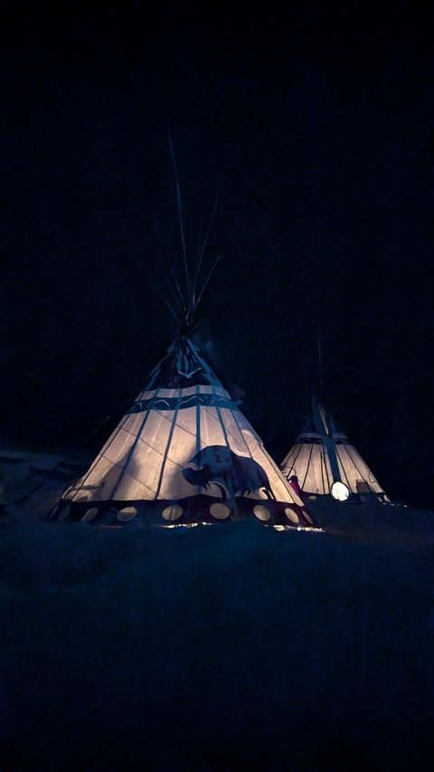 Illuminated traditional teepees glowing warmly against the dark winter night.